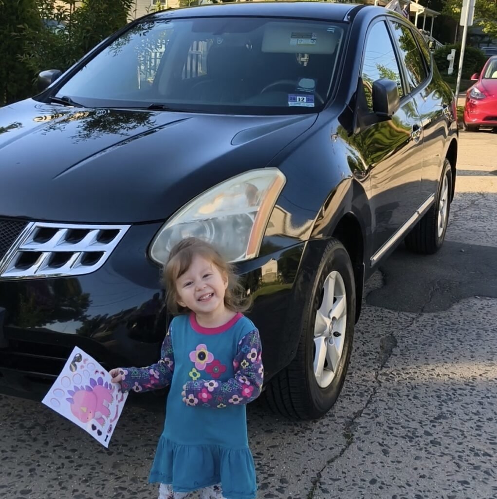 toddler smiling in front of a car